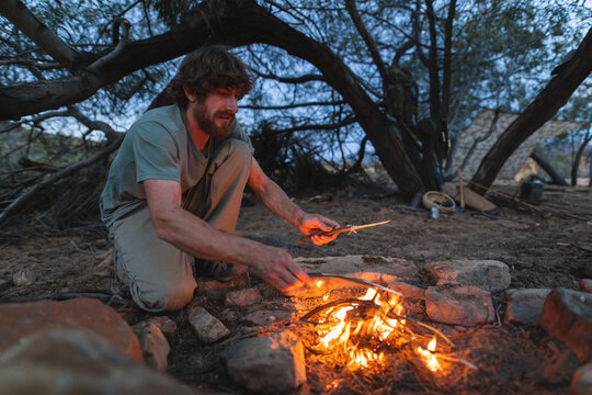 Young male caucasian wanderer burning small firewood sticks while camping in forest