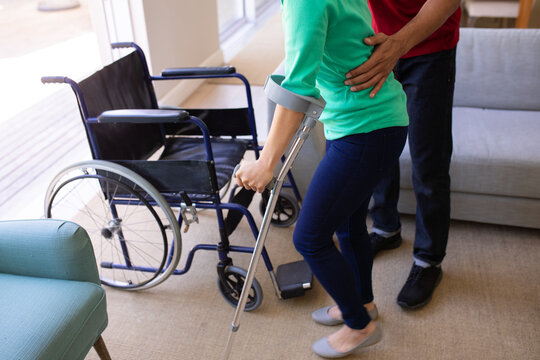 Mid section of african american man helping his disabled wife to walk with crutch at home