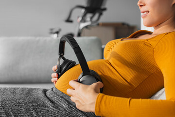 Pregnancy music. Pregnant woman holding headphones to foetus in womb against belly to hear sounds