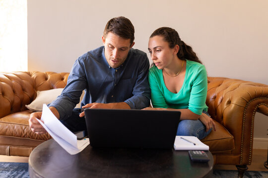 Caucasian couple using laptop and calculating finances together at home