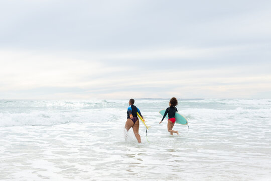 Carefree multiracial female friends with surfboards running in sea against sky during weekend