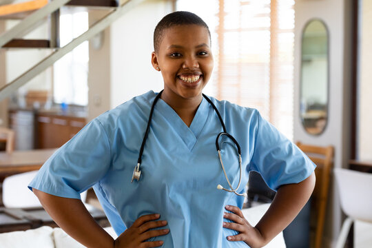 Portrait of smiling african american female doctor in scrubs standing with arms akimbo in hospital