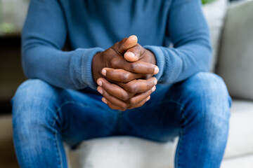 Midsection of african american man sitting on sofa with intertwined fingers at home
