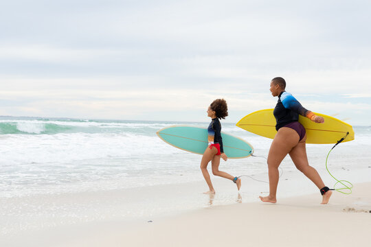 Full length of carefree multiracial female friends with surfboards running at beach during weekend