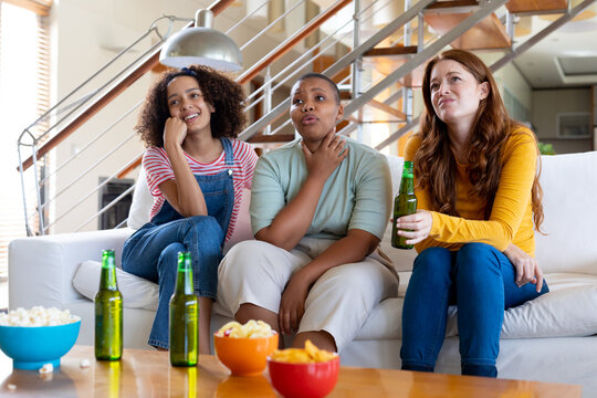 Multiracial female friends with beer and popcorn watching tv at home