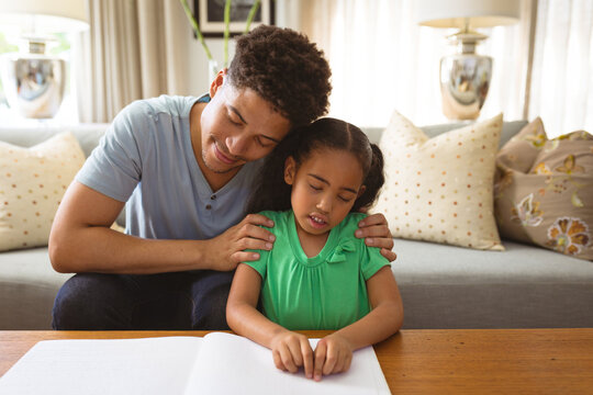 Biracial blind girl touching braille while reading book by father in living room at home