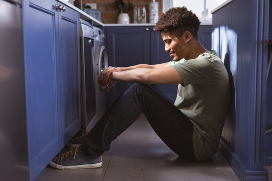 Full length side view of young biracial man sitting in kitchen aisle at home