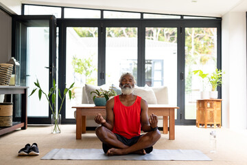 Full length of african american senior man meditating in lotus position practicing yoga at home
