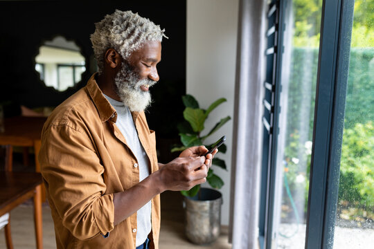 Smiling senior african american man with white beard using mobile phone at home