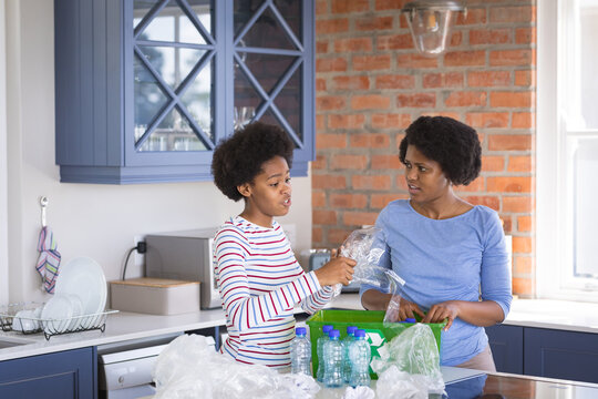 Mother talking with daughter while dumping plastic waste in garbage can at home