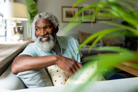 Smiling african american man sitting on sofa while looking over shoulder in living room at home
