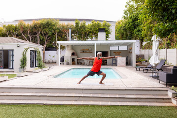 African american senior man practicing warrior pose yoga at poolside