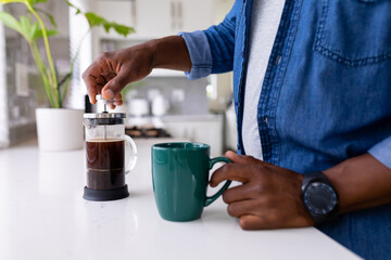 Midsection of senior african american man using french press holding coffee mug at kitchen counter