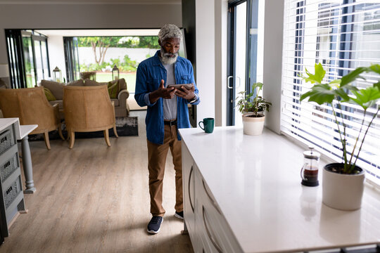 Full length of african american man holding digital tablet standing in living room at home