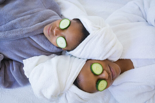 Mother and daughter in bathrobes relaxing with cucumber slices on eyes in spa