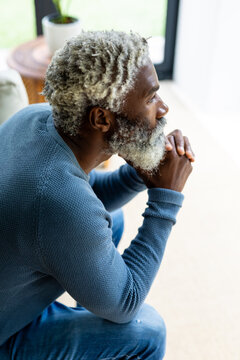Side view of senior african american bearded man with hands on chin thinking in living room at home