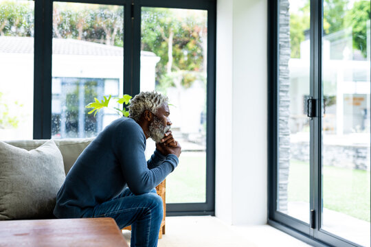 Senior african american man sitting on sofa while thinking in living room at home