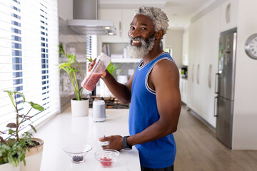 Portrait of smiling african american man with smoothie bottle in kitchen at home