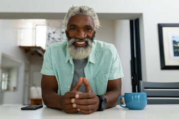 Portrait of smiling senior african american man sitting with coffee mug and smartphone at table