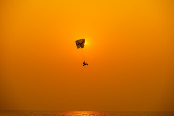 Silhouette of the sport Paramotor control flying through soft sunlight orange sunset sky