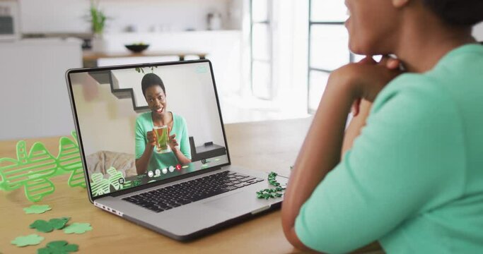 Smiling african american woman with beer wearing clover shape band on video call on laptop