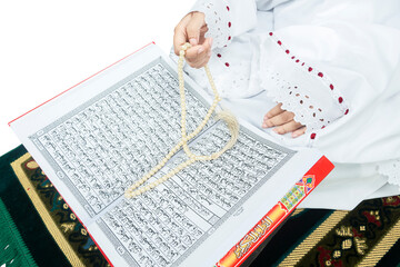 Muslim woman in a veil sitting while raised hands and praying with prayer beads