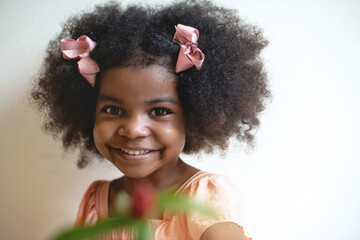 Cute afro little girl with bow wearing old rose color dress, smiling at camera