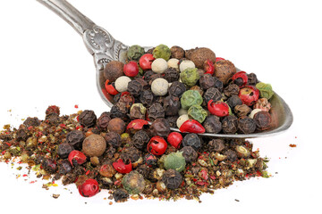 A mixture of whole and ground peppers. Antique silver spoon and pepper isolated on white background