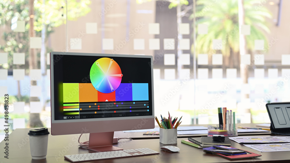 Poster design studio with computer, color swatches and wireframe sketches for mobile application on wooden 