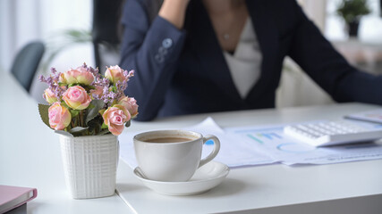 Coffee cup, flower pot and financial documents on white office desk.
