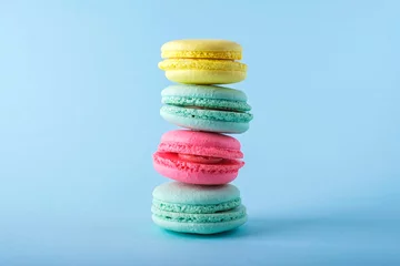 Schilderijen op glas Colorful french macarons cookies (macaroons) on blue background. Dessert, vegetarian sweets close up, stacked balance © Elena
