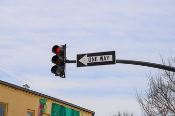 a traffic signal with a red light and a black and white one way sign with blue sky and clouds in...