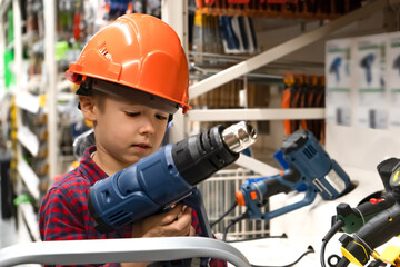 Caucasian boy in a helmet with industrial hair dryer on the stepladder in a hardware store.