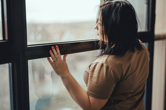 Smiling young woman stands near the observation windows and looks at the city.