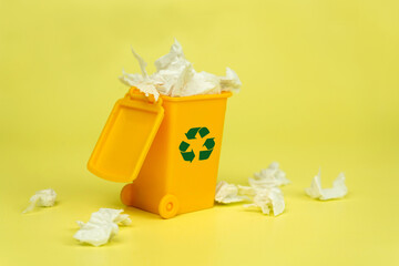 Yellow toy trash can with paper trash with recycling icon