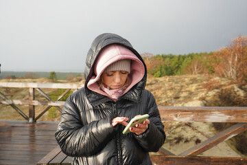 Young girl in a black jacket with a mobile phone on the viewpoint of the Curonian Spit, Kaliningrad.