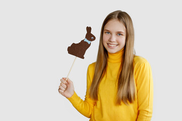 A teenage girl holds a brown felt rabbit in her hands and smiles, a light background, a place for text. Happy Easter, Easter holiday, Easter card