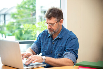 Freelance work. Casual dressed man sitting at wooden desk inside garden working on computer pointing with color pen electronic gadgets dropped around on table side view