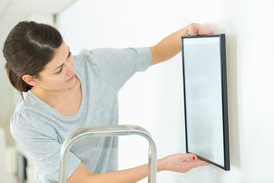 young woman hanging a picture on the wall