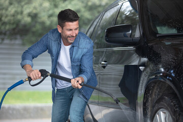 cheerful man using power washer to clean his car