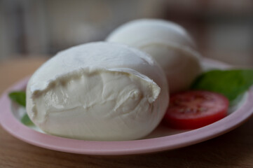 White ball of Italian soft cheese Mozzarella di Bufala Campana with fresh green basil and red tomato