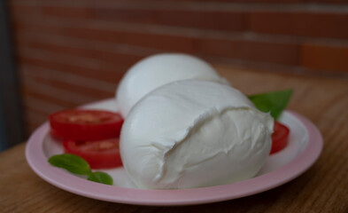 White ball of Italian soft cheese Mozzarella di Bufala Campana with fresh green basil and red tomato