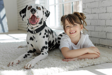 Child with a dog. A happy girl lies on a carpet with a Dalmatian dog. High quality photo