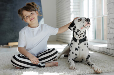 Child with a dog. A happy girl lies on a carpet with a Dalmatian dog. High quality photo