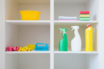 Bowl, brush, detergent bottles, rags, rubber gloves and sponges on white shelves inside opened...