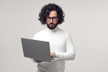 Strict man in eyeglasses typing on laptop in studio