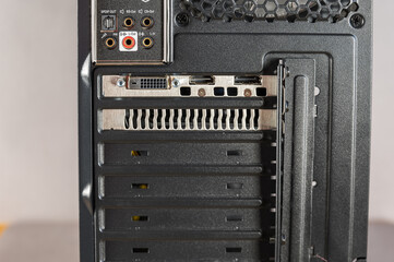 Obraz premium The back of a personal computer system unit. Black metal case with ventilation grille. Connectors for monitor, audio speakers, microphone. Modern digital devices.