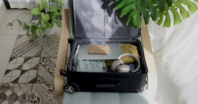 Woman stacking items in a suitcase for a trip. Female hands put a clothes and zip up suitcase at home view from above