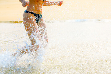 close up leg of young woman running along wave of sea water and sand on the summer beach. Travel...