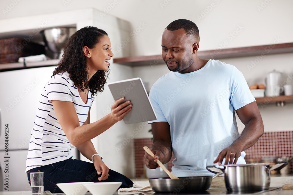 Wall mural Lets see what the cooking app says. Cropped shot of a young married couple using a tablet while cooking together in the kitchen at home.